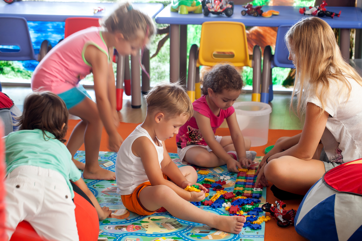 Group of young children playing with toys sitting with an adult woman 