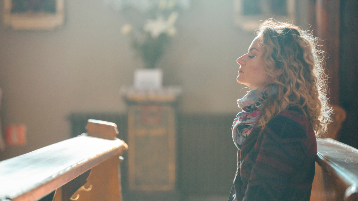 a woman sitting in the pews in church with her eyes closed