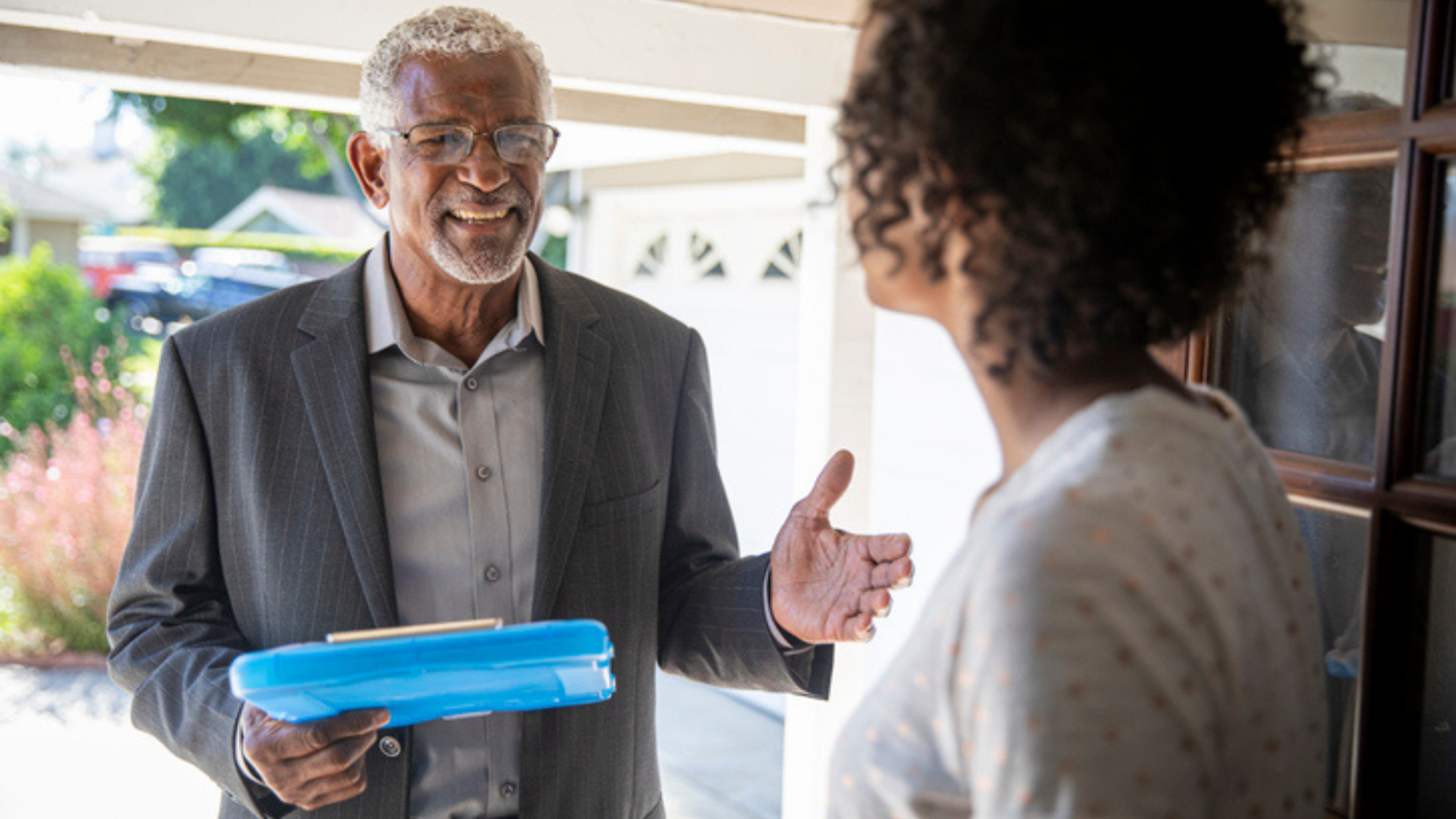 Photo of a man holding a file in his hand speaking to a woman on her front door step