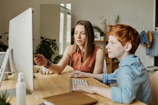 Child using a desktop computer with a women watching