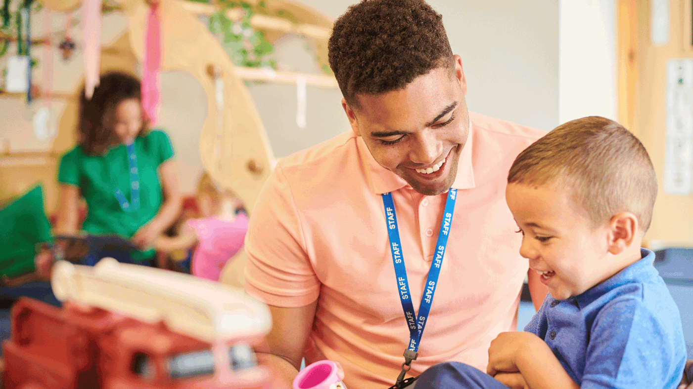 Male kid's worker with small boy in a nursey school setting. Both are smiling.