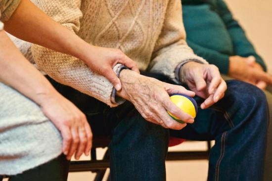 Image of a carer's hand on the arm of an elderly man holding a ball