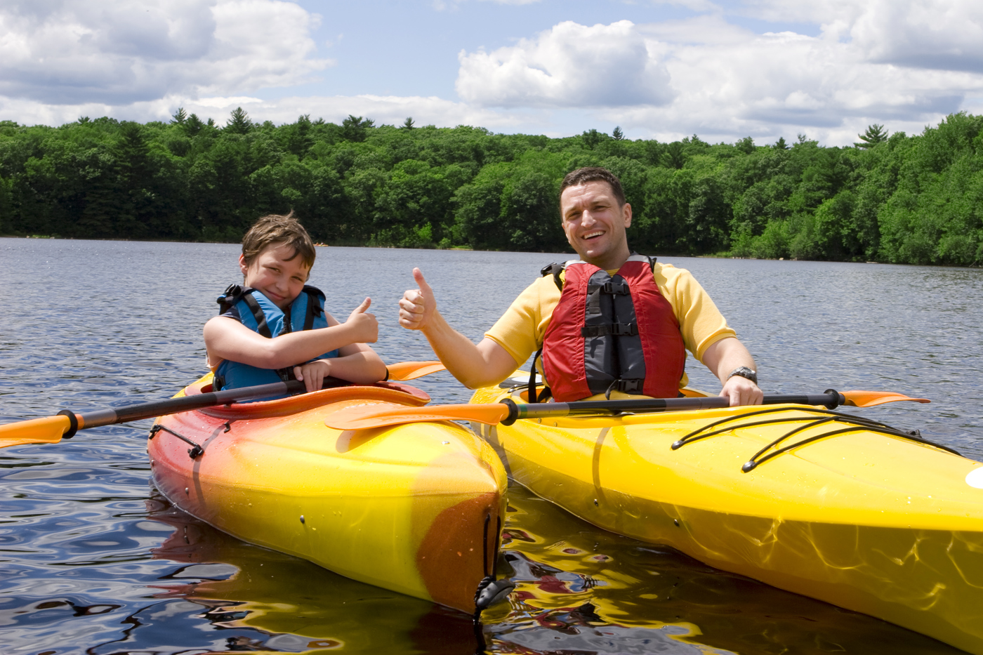 Boy and man in kayaks on water with their thumbs up