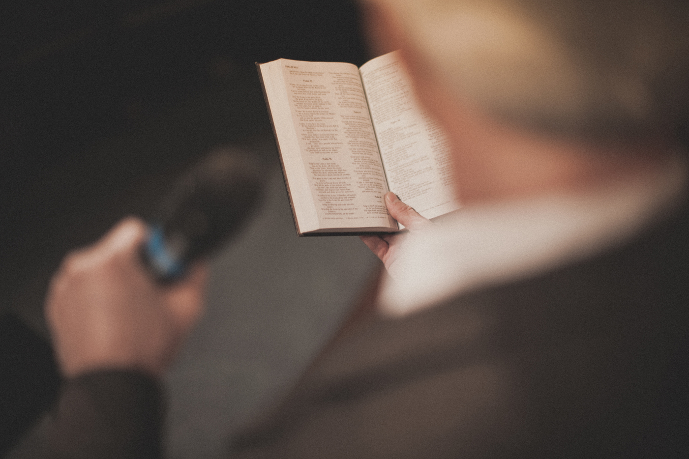 Preacher reading from the bible, holding a microphone, from behind