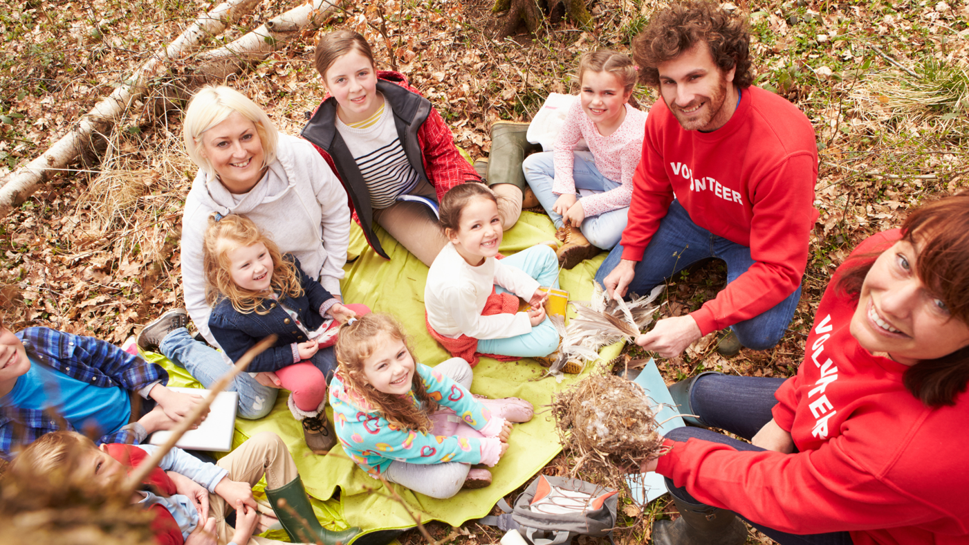 Group of adults and children sitting outdoors with volunteer youth workers