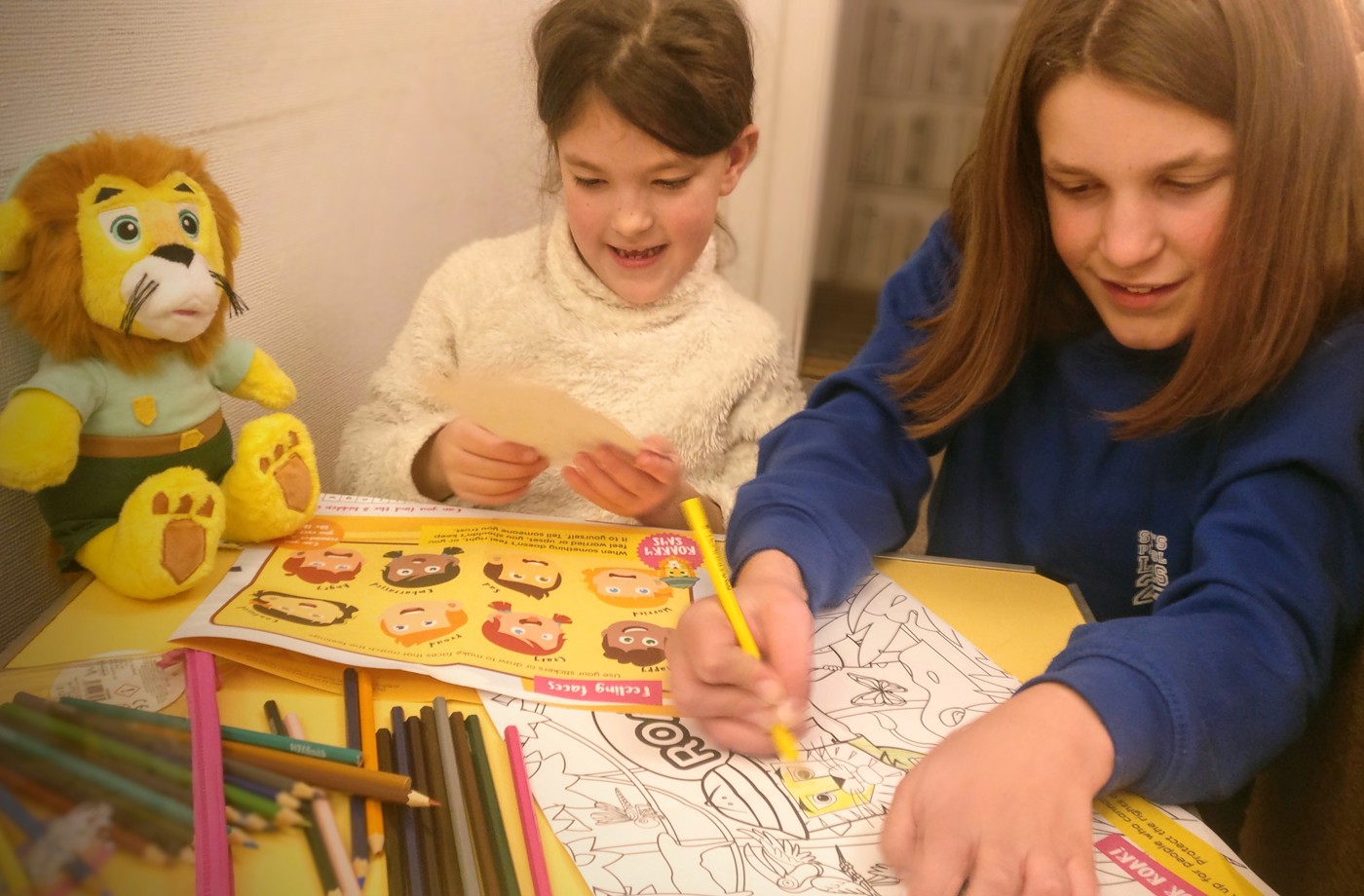 Two girls with a soft plush toy lion doing paper-based activities