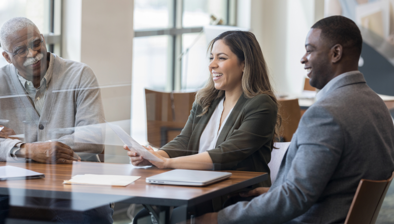 two men and a woman in a board meeting, sitting at a table, smiling